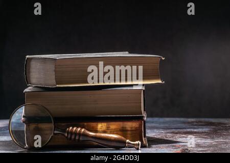 Pile de livres anciens sur une table sur fond sombre et loupe Banque D'Images