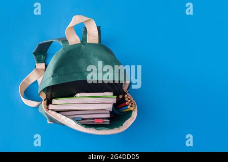 À l'intérieur du sac à dos vert se trouvent des livres, des carnets et des crayons sur fond bleu. Banque D'Images