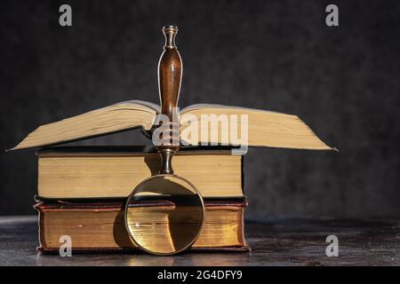 Pile de livres anciens sur une table sur fond sombre et loupe Banque D'Images