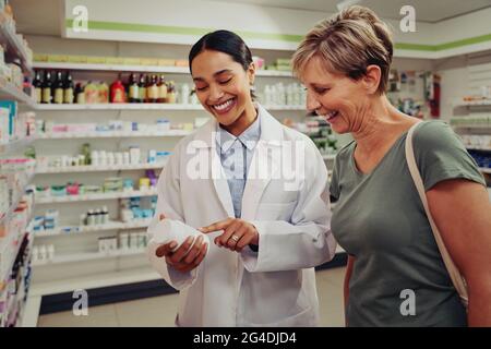 Une jeune pharmacienne et une cliente lisant les ingrédients et le dosage dans une pharmacie située près des étagères Banque D'Images