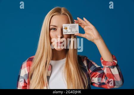 Blonde heureuse femme blanche faisant des lèvres de baiser tout en montrant la carte de crédit isolée sur fond bleu Banque D'Images