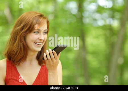 Une femme heureuse utilisant la reconnaissance vocale sur un smartphone situé dans une forêt Banque D'Images