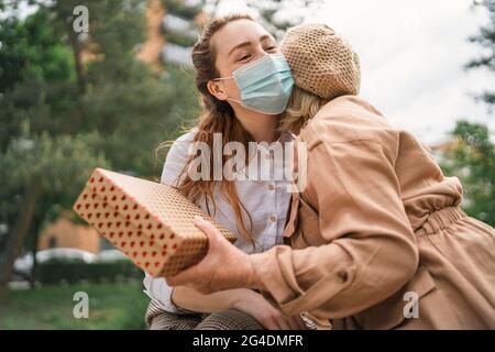 Jeune femme donnant la grand-mère présente et embrassant à l'extérieur dans la ville, la vie après la vaccination Covid-19. Banque D'Images