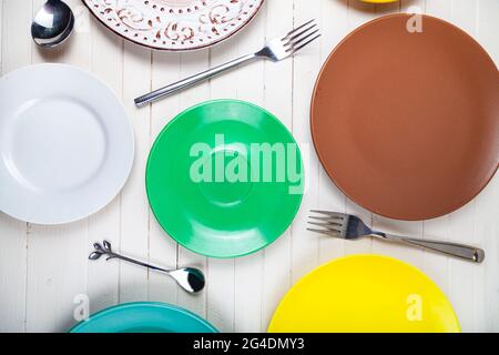 Vider les assiettes, cuillères et fourchettes multicolores sur fond de bois, vue du dessus. Banque D'Images