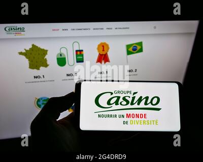 Personne tenant un smartphone avec le logo de la société de vente au détail française Casino Guichard-Perrachon S.A. à l'écran devant le site. Mise au point sur l'affichage du téléphone. Banque D'Images
