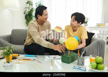 Père parlant de planètes en faisant le modèle du système solaire avec son fils pour l'école Banque D'Images