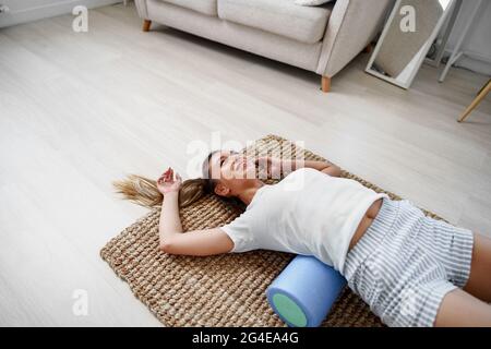 Jeune femme faisant de l'exercice avec le rouleau de gymnastique sur le sol à la maison Banque D'Images