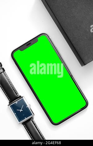 IPhone à écran vert sur une table blanche avec montre-bracelet et livre de notes Banque D'Images