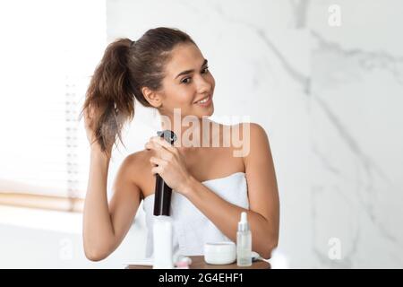 Gaie femme en train de vaporiser un spray à la queue de cheval dans la salle de bains intérieure Banque D'Images