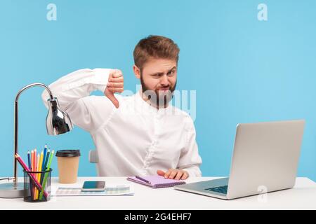 Je n'aime pas ! Un employé mécontent, assis au bureau, a fait preuve d'un geste de la main, exprimant sa désapprobation et une note de service négative. Studio intérieur Banque D'Images