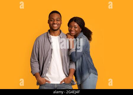 Joyeux jeune couple afro-américain en vêtements décontractés posant sur fond jaune Banque D'Images