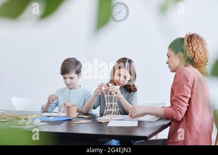 Vue latérale portrait d'une enseignante aidant les enfants à faire des maquettes en bois pendant les cours d'art et d'artisanat à l'école, espace de copie Banque D'Images