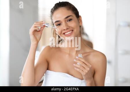 Bonne femme appliquant le sérum facial avec le compte-gouttes peau hydratante intérieure Banque D'Images