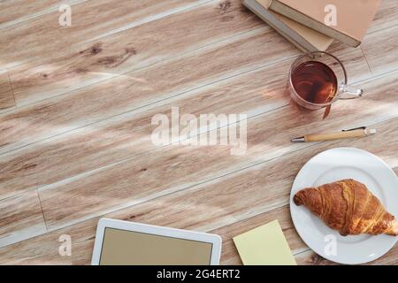 Arrière-plan du bureau avec une tasse de thé et un croissant, un ordinateur de table et des livres Banque D'Images