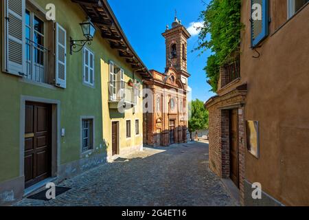 Rue pavée étroite entre maisons et vieille église en brique sous ciel bleu dans le Piémont, dans le nord de l'Italie. Banque D'Images