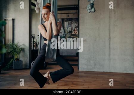 Jeune femme mince avec les cheveux rouges pratique anti-gravité Fly yoga Banque D'Images