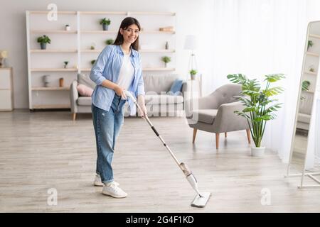 Portrait d'une femme gaie qui nettoie le sol avec une vadrouille vaporisée Banque D'Images