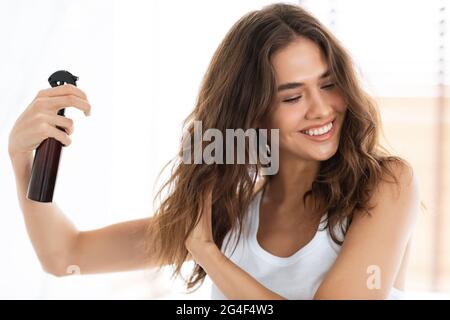 Bonne femme appliquant du spray sur les cheveux ondulés dans la salle de bains moderne Banque D'Images