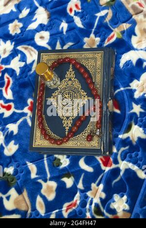 Livre islamique Saint Coran avec roseaux et bouteille de parfum sur tapis de prière coloré, concept de foi religieuse musulmane Banque D'Images