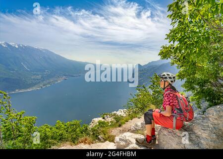 Belle femme âgée avec casque de vélo se reposant à Punta Larici et appréciant la vue magnifique sur le lac de Garde entre Riva del Garda et Torbole, Italie Banque D'Images