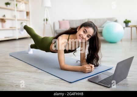 Femme indienne forte debout dans le coude de planche devant l'ordinateur portable, de l'activité sur le tutoriel de sport en ligne à la maison Banque D'Images