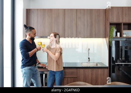Joyeux jeune couple en train de griller avec des verres de vin en célébrant le déménagement dans un nouvel appartement Banque D'Images