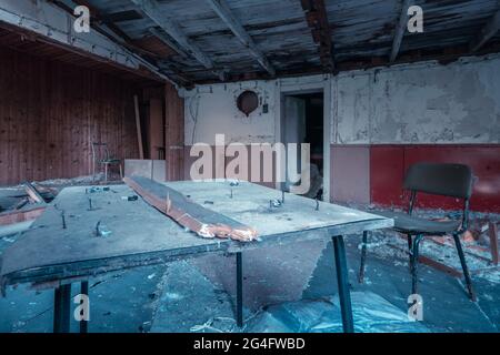 Table sale avec de vieux ongles dans elle et une chaise dans la pièce désordonnée d'une vieille maison abandonnée en train de tomber en morceaux Banque D'Images