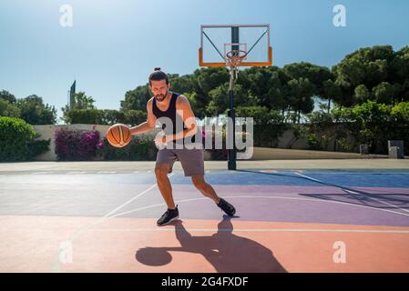 FIT homme jouant au basket-ball extérieur, temps ensoleillé, terrain de jeu moderne Banque D'Images