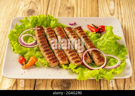 Chevapchichi, un hors-d'œuvre de viande sur une table en bois. Des feuilles de laitue et du piment complètent le plat à viande. Lula-Kebab. Mise au point sélective. Banque D'Images