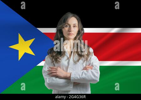 Médecine au Soudan du Sud. Heureuse belle femme médecin en manteau médical debout avec des bras croisés sur le fond du drapeau du Sud Soudan. Banque D'Images