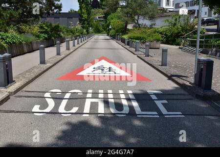 Signe d'avertissement de la voie à l'école en langue allemande en Suisse. Le panneau de signalisation est triangle rouge avec les enfants en cours d'exécution dans le champ blanc et le texte Schule. Banque D'Images