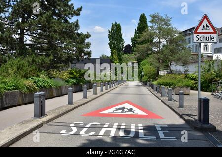 Panneau d'avertissement sur une route et panneau de signalisation vertical sur le chemin de l'école en langue allemande en Suisse. Le panneau de signalisation est triangle rouge avec les enfants en train de courir i Banque D'Images