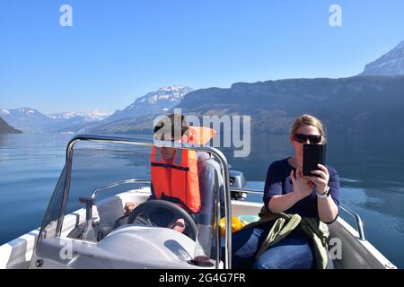 Mère et fils en bateau à moteur sur le lac de Lucerne en Suisse. Garçon porte un gilet de sauvetage et des lunettes de soleil orange. La femme fait des photos. Banque D'Images