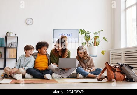 Divers groupes d'enfants assis sur le sol à l'école avec une enseignante souriante Banque D'Images