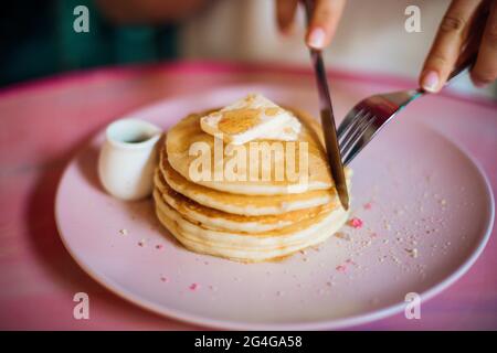 La jeune femme coupe un morceau de la pile de crêpes sucrées avec du fromage doux ou du beurre trempé dans le miel. Desserts sucrés.concept de nutrition appropriée. Fait maison Banque D'Images