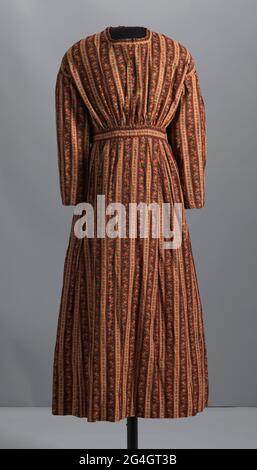 Cette robe à manches longues et coutures à la main est réalisée dans un coton imprimé à tissage Uni équilibré. Les manches sont rassemblées au niveau de la couture arrière de l'épaule et la couture de l'épaule est tombée dans le dos. Le corsage est rassemblé à la taille avant et a une bande de cou sans col. La bande de cou et la bande de taille sont difficiles à mettre en valeur le motif imprimé. Des passepoil sont fixés au niveau des emmanchures et le long du bas de la taille. La jupe est rassemblée sur les hanches avant et arrière avec un panneau plat le long de la taille centrale avant. Sur le corsage arrière approprié, trois (3) boutons en verre sont cousus Banque D'Images