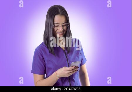 Jeune médecin/infirmière hispanique gaie portant des lunettes à l'aide de son smartphone Banque D'Images