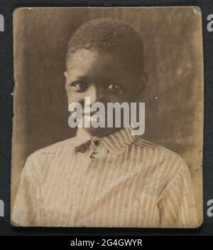 Une photographie en noir et blanc d'un jeune garçon. Le garçon est présenté de la poitrine vers le haut et regarde directement la caméra. Il porte une chemise boutonnée à col rayé. Le verso de la photo est vide. Banque D'Images