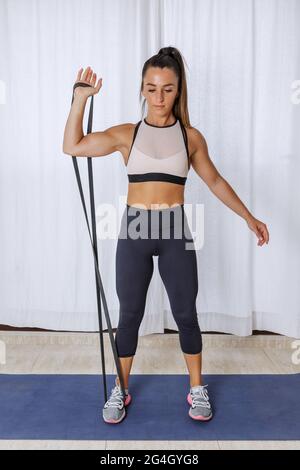 Corps complet de la jeune femme dans les vêtements de sport faisant un bras bicep curl exercice avec corde de résistance pendant l'entraînement de fitness à la maison Banque D'Images
