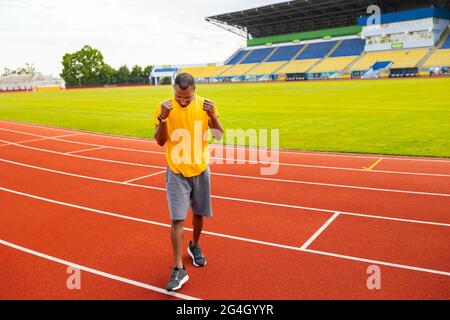 Joyeux jeune afro-américain dans sportswear triomphant souriant célébrant but, match gagner criant avec joie sur le fond du stade, heureux Banque D'Images