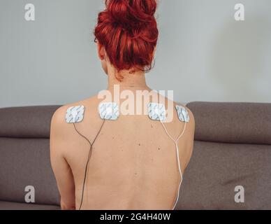 Femme en thérapie avec des électrodes placées sur les muscles du dos, réadaptation post-traumatique, traitement Banque D'Images