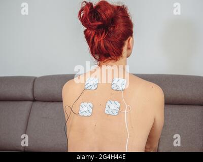 Femme en thérapie avec des électrodes placées sur les muscles du dos, réadaptation post-traumatique, traitement Banque D'Images