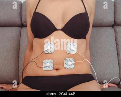 Femme en thérapie avec des électrodes placées sur les muscles abdominaux, réadaptation post-traumatique, traitement Banque D'Images