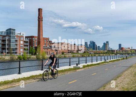 Montréal, CA - 15 mai 2021 : homme faisant du vélo sur la piste cyclable du canal de Lachine, avec une ligne d’horizon en arrière-plan. Banque D'Images