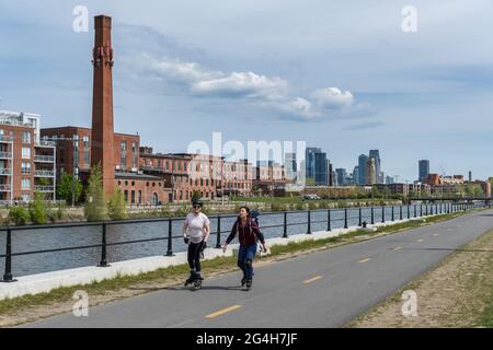 Montréal, CA - 15 mai 2021 : les gens patinent sur la piste cyclable du canal de Lachine, avec un horizon à l’arrière-plan. Banque D'Images