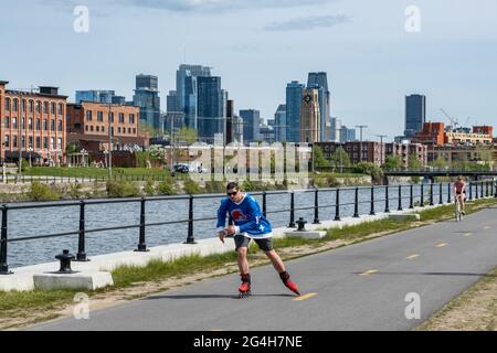 Montréal, CA - 15 mai 2021 : patinage d’homme sur la piste cyclable du canal de Lachine, avec une ligne d’horizon en arrière-plan. Banque D'Images