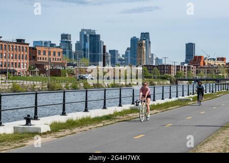 Montréal, CA - 15 mai 2021 : une femme fait du vélo sur la piste cyclable du canal de Lachine, avec un horizon à l’arrière-plan. Banque D'Images