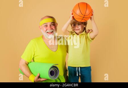 Sport familial. Grand-père avec tapis de yoga et enfant avec ballon de basket-ball. Grand-père et petit-fils sportifs. Banque D'Images