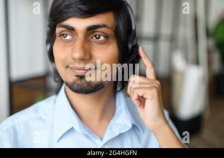 Un homme indien souriant qui porte un casque prend un appel, parle avec des clients ou des collègues, un représentant de l'assistance à l'intérieur, un coup de tête d'un employé hindou qui touche un casque Banque D'Images