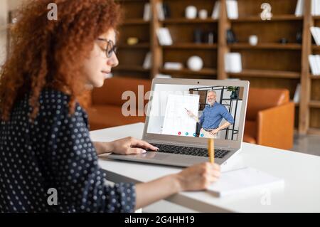 Concept d'étude électronique. Une étudiante curieuse regardant un webinaire éducatif en ligne, écoutant un enseignant senior avec un tableau blanc à l'écran, se préparant aux examens en ligne, prend des notes Banque D'Images